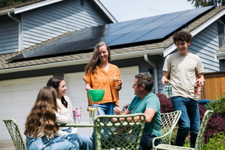 Family Enjoying Snack Outdoors in Front of Solar Equipped Home